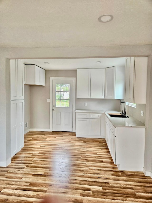 kitchen featuring light wood-style flooring, baseboards, a sink, and white cabinetry