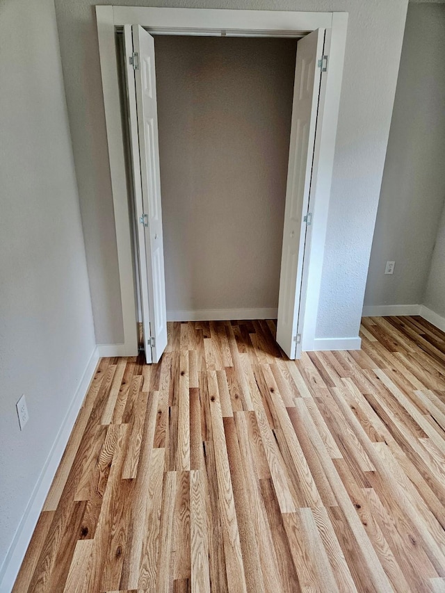 unfurnished bedroom with light wood-style flooring, a closet, and baseboards