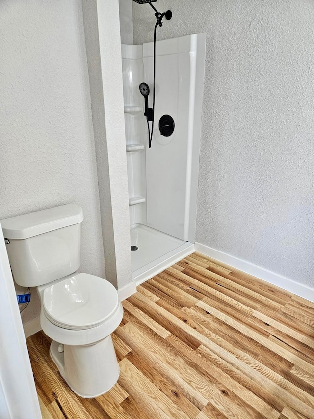 full bathroom with toilet, a textured wall, wood finished floors, and a shower
