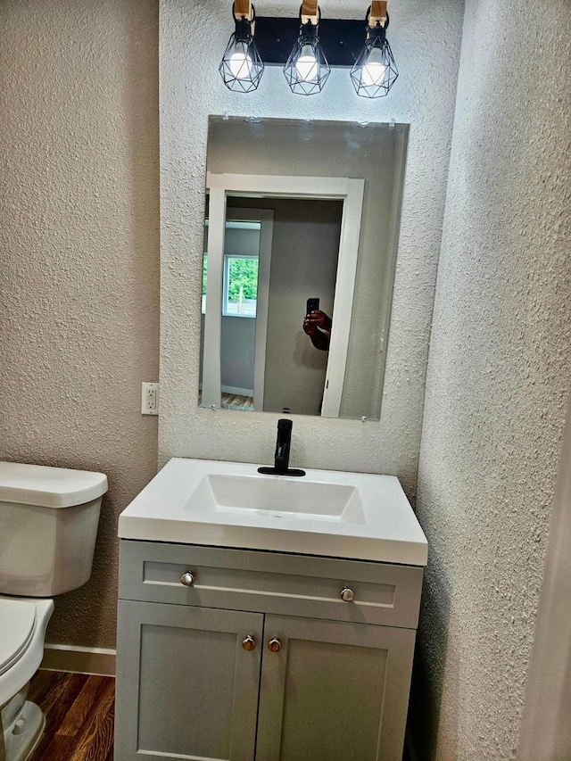 bathroom featuring wood finished floors, vanity, a textured wall, baseboards, and toilet