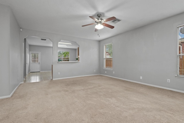 empty room featuring ceiling fan, light carpet, visible vents, and a wealth of natural light