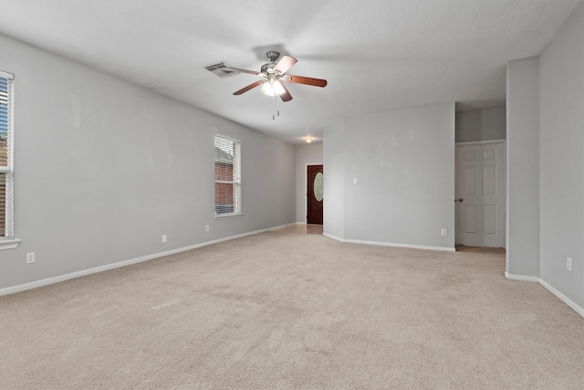spare room featuring light carpet, a ceiling fan, visible vents, and baseboards