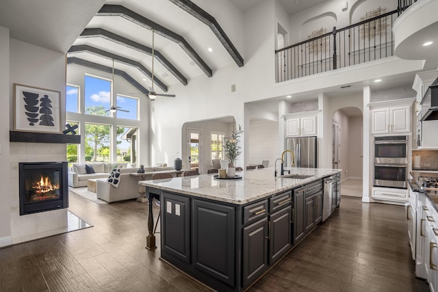 kitchen with appliances with stainless steel finishes, arched walkways, a sink, white cabinets, and open floor plan