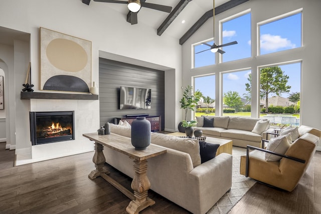living area featuring ceiling fan, high vaulted ceiling, a glass covered fireplace, wood finished floors, and beamed ceiling