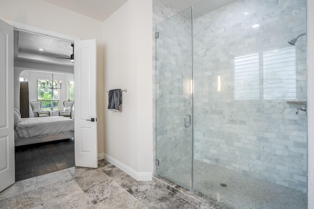 bathroom with ceiling fan with notable chandelier, baseboards, a shower stall, and ensuite bath