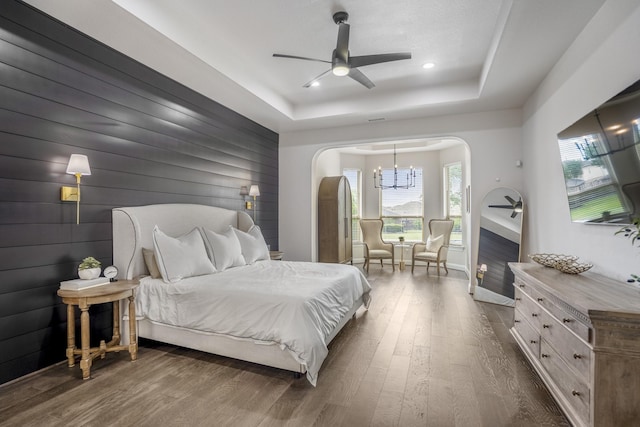 bedroom featuring baseboards, dark wood-type flooring, recessed lighting, a tray ceiling, and arched walkways