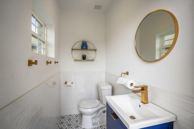 bathroom featuring vanity, a wainscoted wall, toilet, and tile walls