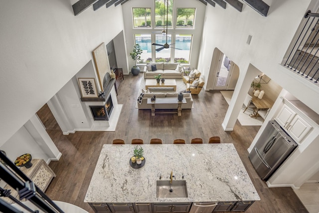 living area with a ceiling fan, baseboards, dark wood-style floors, and a towering ceiling