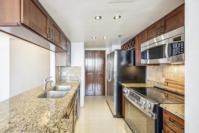 kitchen featuring stainless steel appliances, light tile patterned floors, a sink, light stone countertops, and tasteful backsplash