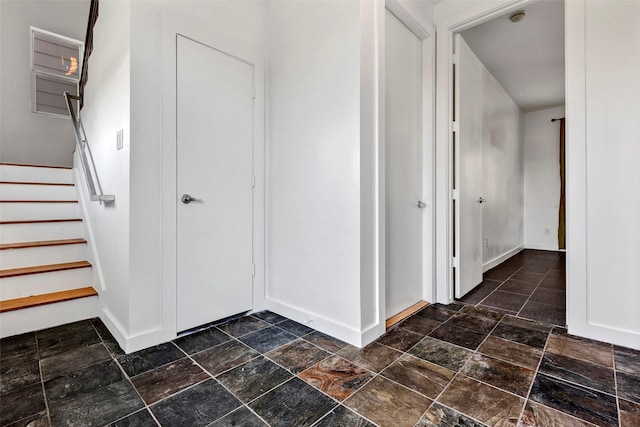 hallway featuring stone tile floors, baseboards, and stairway