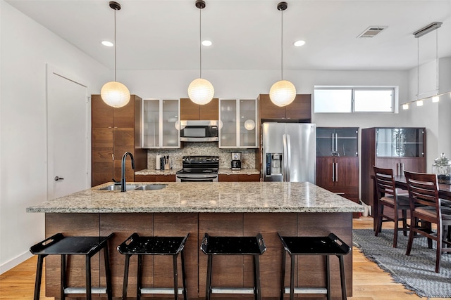 kitchen with visible vents, light wood-type flooring, tasteful backsplash, a sink, and appliances with stainless steel finishes