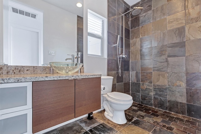 bathroom featuring toilet, visible vents, a tile shower, and vanity
