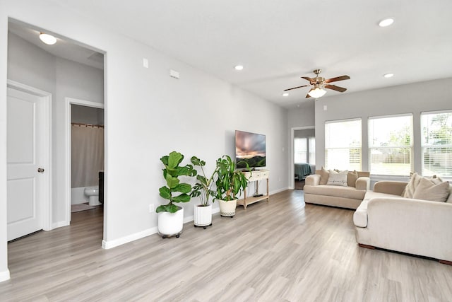 living room with light wood-style floors, baseboards, ceiling fan, and a wealth of natural light