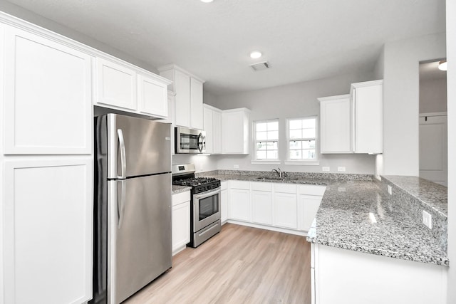 kitchen with visible vents, white cabinetry, light stone counters, light wood-style flooring, and appliances with stainless steel finishes