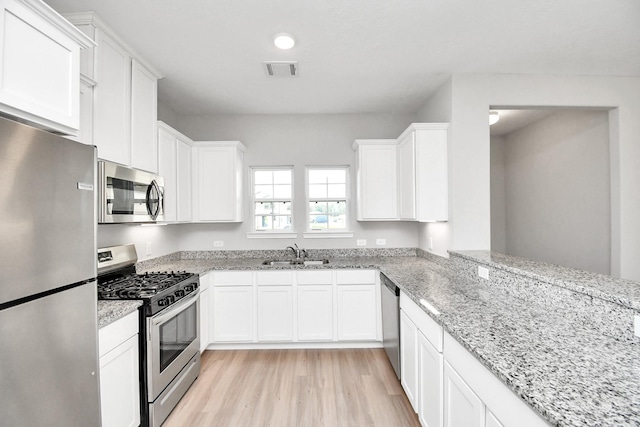 kitchen featuring visible vents, appliances with stainless steel finishes, a sink, light wood finished floors, and white cabinetry