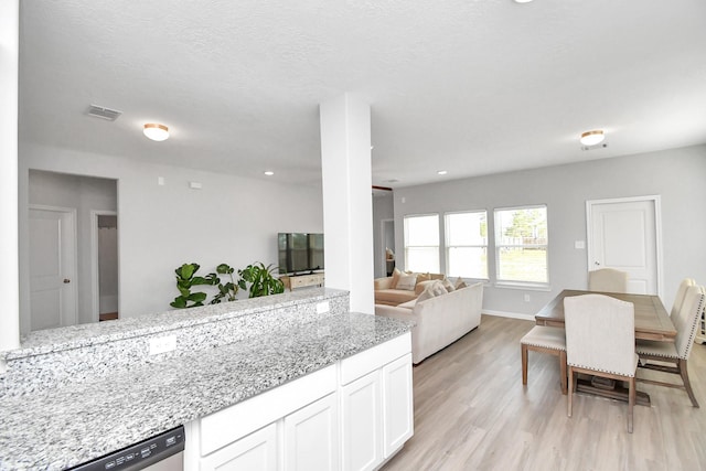 kitchen with visible vents, light stone countertops, stainless steel dishwasher, light wood-type flooring, and white cabinets