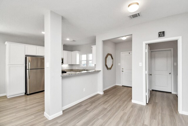 kitchen with light wood-style floors, freestanding refrigerator, white cabinetry, baseboards, and visible vents