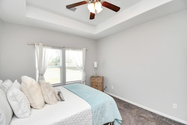 carpeted bedroom with baseboards, a ceiling fan, a tray ceiling, and visible vents