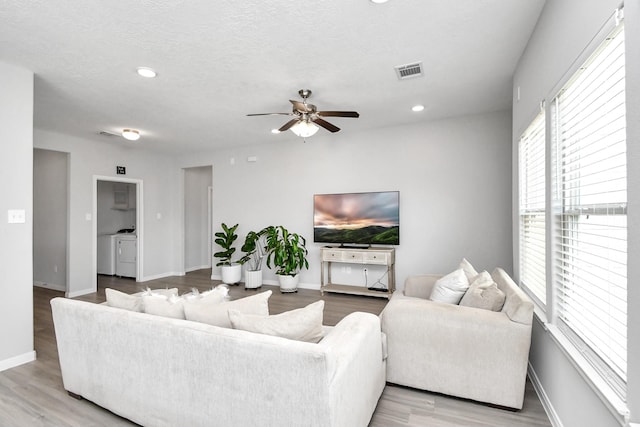 living room with visible vents, a ceiling fan, light wood finished floors, and washer and clothes dryer