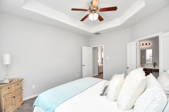 bedroom with a ceiling fan, visible vents, baseboards, a tray ceiling, and ensuite bath