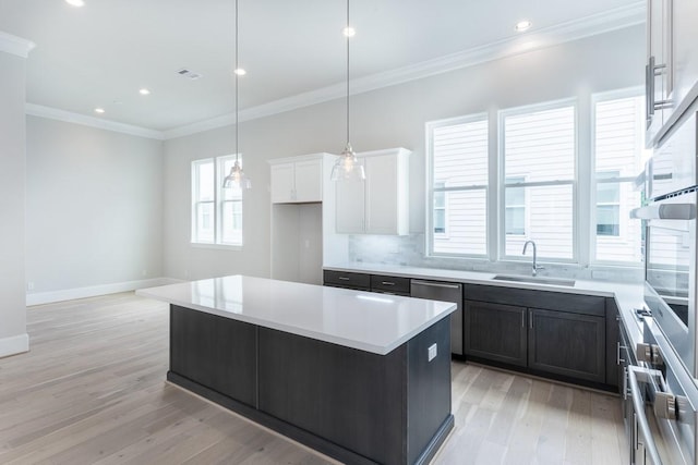 kitchen with white cabinets, a sink, crown molding, light wood-style flooring, and appliances with stainless steel finishes