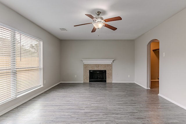 unfurnished living room with arched walkways, a ceiling fan, wood finished floors, and a tile fireplace