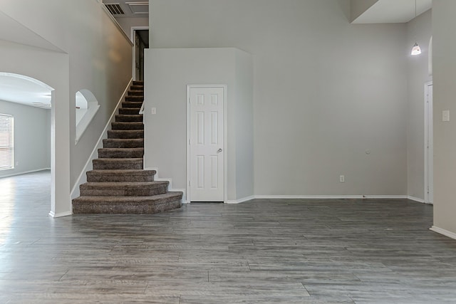 interior space featuring a towering ceiling, wood finished floors, baseboards, stairway, and arched walkways