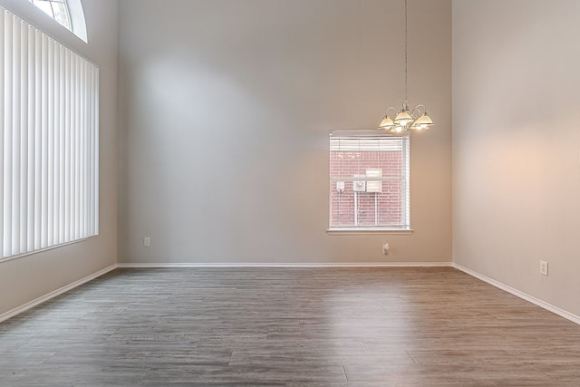 spare room with an inviting chandelier, a high ceiling, baseboards, and wood finished floors