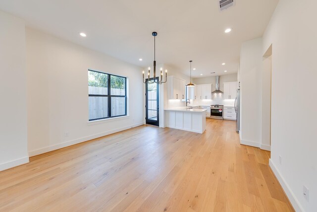 interior space featuring wall chimney exhaust hood, stainless steel appliances, a sink, visible vents, and light countertops