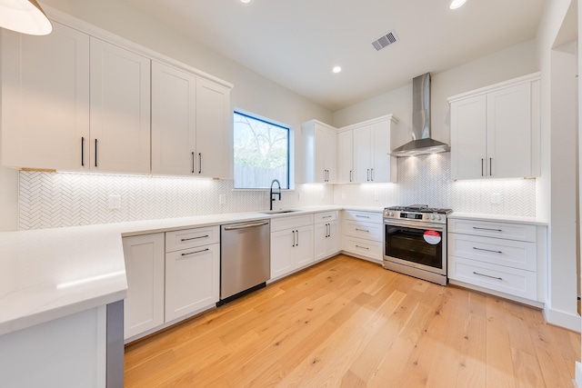 kitchen with wall chimney exhaust hood, stainless steel appliances, a sink, white cabinetry, and light countertops