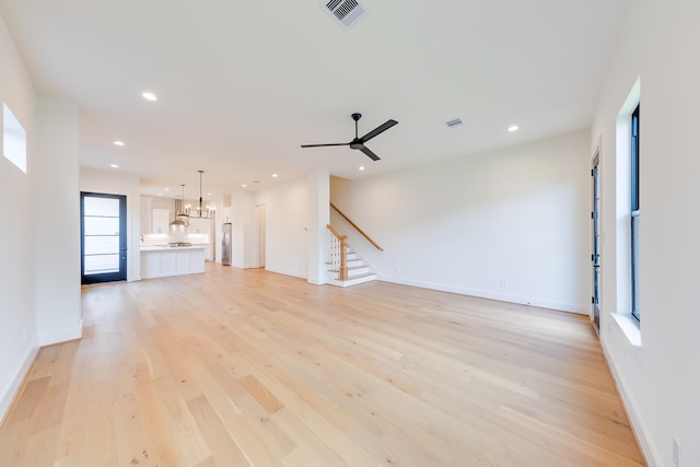 unfurnished living room with light wood-style floors, visible vents, stairs, and ceiling fan with notable chandelier