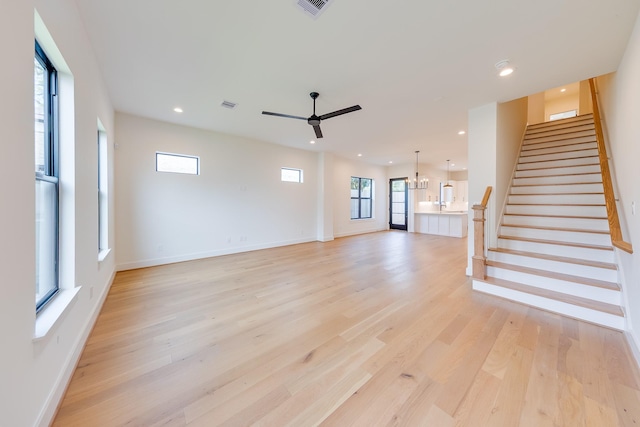 unfurnished living room with recessed lighting, light wood finished floors, stairs, and ceiling fan with notable chandelier
