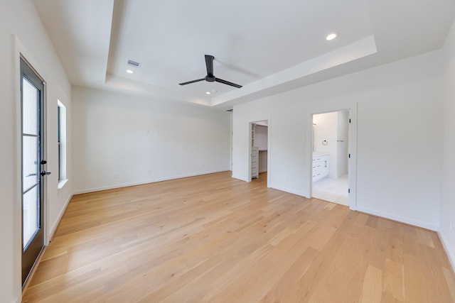 unfurnished bedroom featuring light wood-style flooring, baseboards, a raised ceiling, and multiple windows