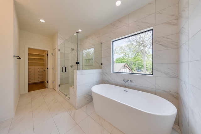 bathroom featuring a shower stall, marble finish floor, a freestanding bath, a walk in closet, and tile walls