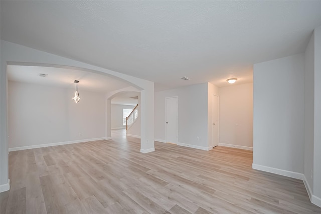 unfurnished living room with arched walkways, stairway, light wood finished floors, and baseboards