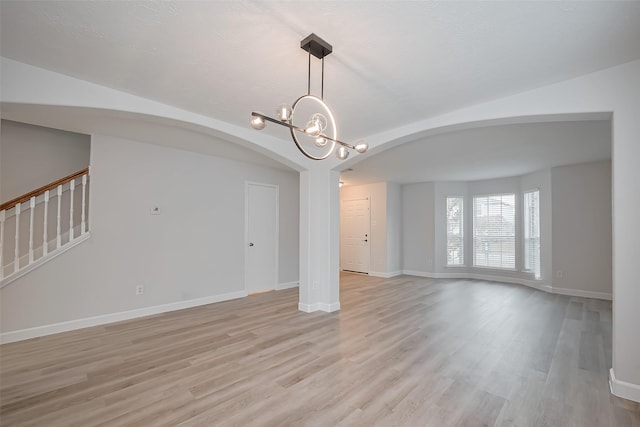 interior space featuring arched walkways, light wood-style floors, baseboards, and a notable chandelier