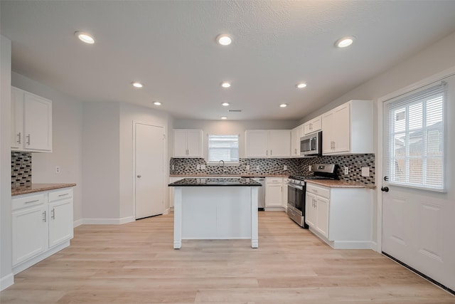 kitchen with white cabinets, stainless steel appliances, light wood-style floors, and backsplash