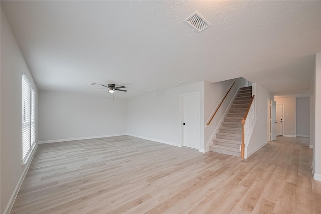 unfurnished living room featuring visible vents, baseboards, light wood-style flooring, stairs, and ceiling fan