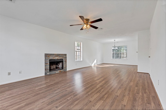 unfurnished living room with baseboards, visible vents, ceiling fan with notable chandelier, wood finished floors, and a fireplace