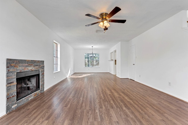 unfurnished living room featuring ceiling fan with notable chandelier, baseboards, a stone fireplace, and wood finished floors