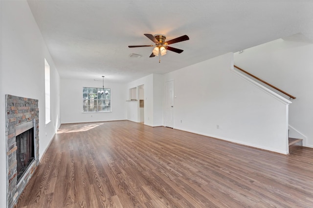 unfurnished living room featuring stairs, wood finished floors, ceiling fan with notable chandelier, a fireplace, and baseboards
