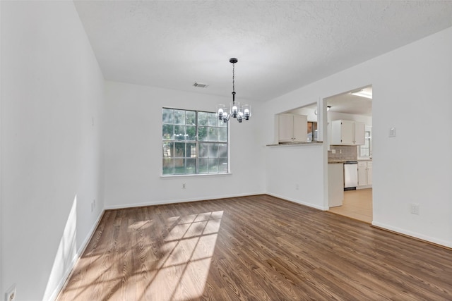 unfurnished dining area with an inviting chandelier, wood finished floors, visible vents, and baseboards