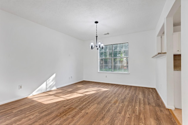 unfurnished dining area with wood finished floors, visible vents, baseboards, and an inviting chandelier