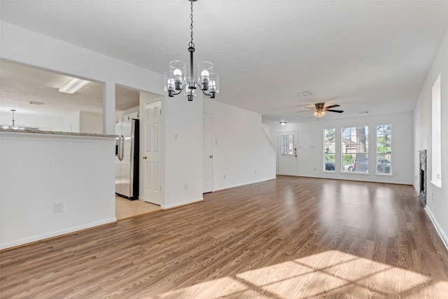 unfurnished living room featuring light wood finished floors, baseboards, and ceiling fan with notable chandelier