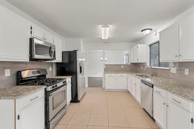 kitchen with white cabinets, stainless steel appliances, a sink, light tile patterned flooring, and tasteful backsplash