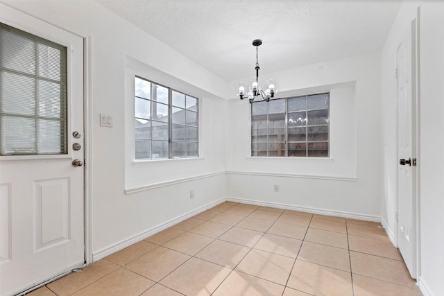 unfurnished dining area featuring baseboards, a textured ceiling, a notable chandelier, and light tile patterned flooring