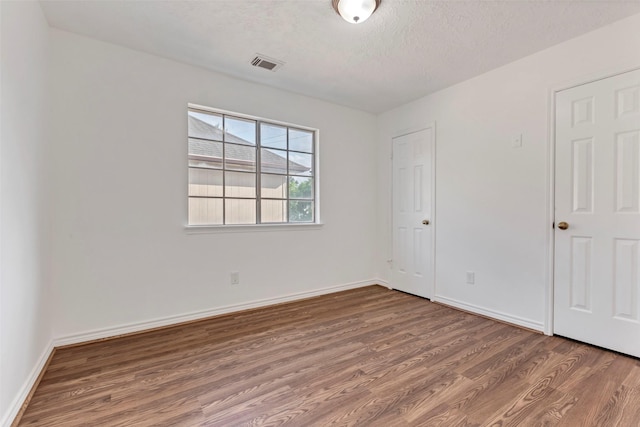 unfurnished bedroom featuring baseboards, wood finished floors, visible vents, and a textured ceiling