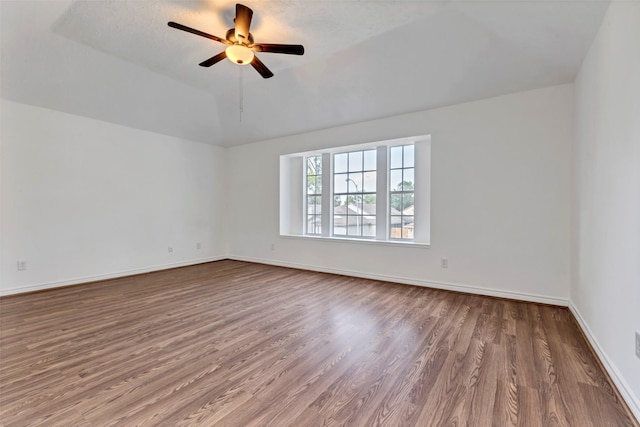 empty room featuring lofted ceiling, baseboards, wood finished floors, and ceiling fan