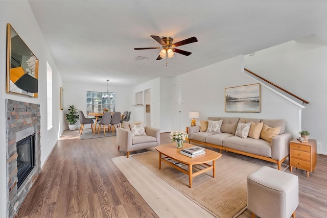 living area with wood finished floors, visible vents, baseboards, a glass covered fireplace, and ceiling fan with notable chandelier