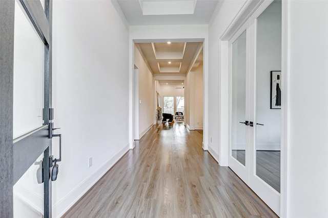hallway featuring a raised ceiling, light wood finished floors, and baseboards